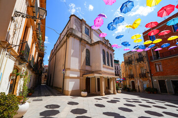Piazza Pichi, Iglesias, Sardinia, featuring the historic Teatro Electra beneath a colorful canopy of hanging umbrellas © Alexandre ROSA