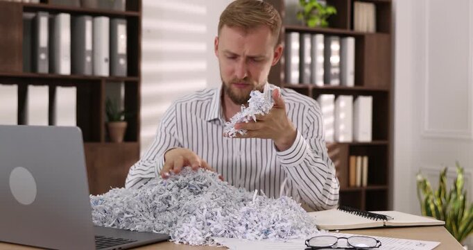 Man with shredded paper pieces at table in office, selective focus