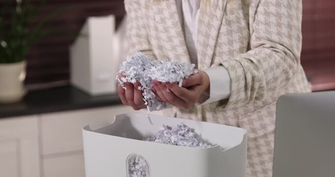 Woman taking out cut paper pieces from shredder bin in office, closeup