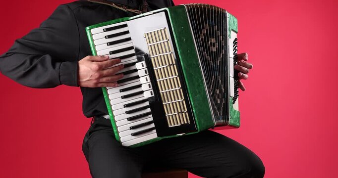 Man playing piano accordion on red background, closeup