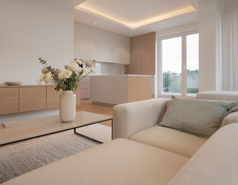 A close-up of a very modern living room featuring simple, concealed modern lighting and floral accents; the new furniture avoids a futuristic look, complementing the open-plan layout shared with the k
