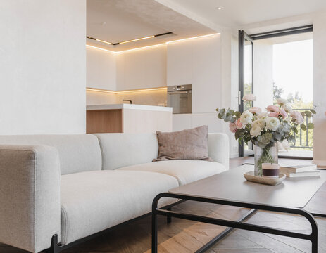 A close-up of a very modern living room featuring simple, concealed modern lighting and floral accents; the new furniture avoids a futuristic look, complementing the open-plan layout shared with the k