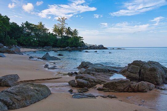 Secluded rocky cove with palm trees and calm sea at Banana Beach, Phuket, Thailand