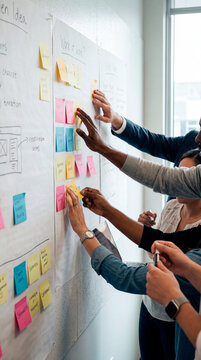 Diverse team hands placing colorful sticky notes on whiteboard during brainstorming session