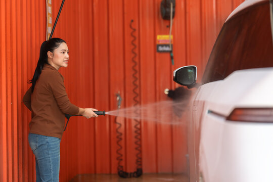 woman washing car with water hose in a self-service car wash station