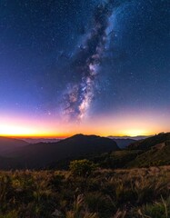 Fototapeta premium The Milky Way galaxy arches over a twilight mountain landscape, with the last light of sunset on the horizon.