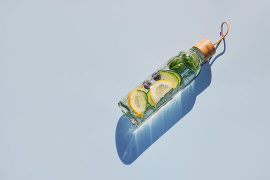 Reusable glass bottle containing refreshing detox water with cucumber, lemon, blueberry and basil