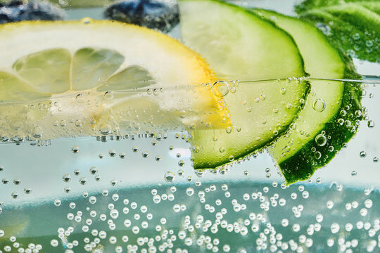 Refreshing lemon and cucumber slices gently immersed in sparkling effervescent water with rising bubbles