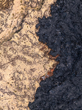 Aerial view of the stark contrast between light-colored mossy terrain and dark, solidified black lava flow in the volcanic landscape of Iceland.