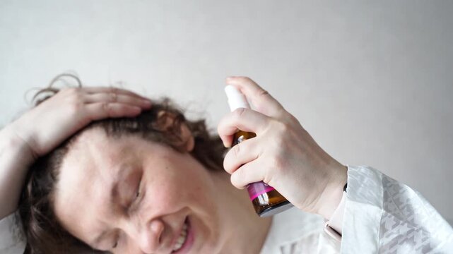 Handheld Closeup Of Woman Spraying Hair Treatment Onto Scalp And Massaging Messy Hair During Personal Grooming Routine In Bright Home Bathroom.