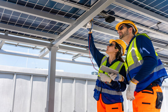 Team of electrical engineers inspecting solar panels with tablet and multimeter, Professional technicians performing maintenance check on solar energy system