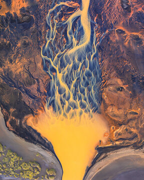 Aerial view of a glacial river delta in Iceland, showing intricate braided river patterns with vibrant yellow sediment and dark volcanic sand.