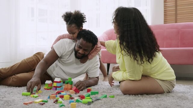 Family day concept. Happy African American father, mother, and child daughter sitting and playing with multicolored wooden blocks together with love and bonding on the floor in the living room at home