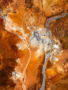 Aerial view of vibrant geothermal landscape with orange and red mineral deposits, steaming vents, and volcanic soil patterns in Iceland.