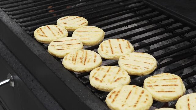 Fresh traditional Colombian arepas cooking on a charcoal grill, showing distinctive golden grill marks