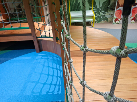 lose-up shot of a grey rope climbing net installation alongside curved horizontal wooden steps within an indoor kids' play park.