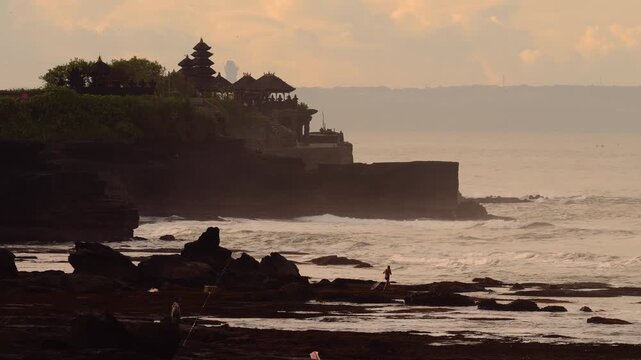 Sunset Coastline Tanah Lot Temple Silhouette In Bali Golden Light Washes Ancient Shrine Perched On Rugged Cliff, Waves Breaking Against Rocky Shore, Mist Rising, Tranquil Mood, Bali