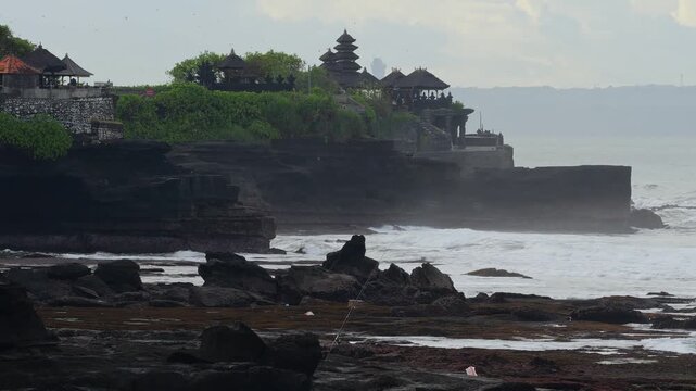 Rugged Rock Stacks With Pounding Surf, Breaking Against Jagged Outcrops, Misty Spray And Foam, Distant Temple Silhouette On Clifftop, Raw Coastal Energy And Exploration Vibe, Tanah Lot temple, Bali