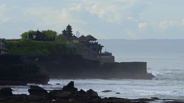 Calm Sunrise Over Tranquil Tanah Lot Temple Setting. Early Morning Mist Surrounds Silhouetted Temple On Cliff Edge. Gentle Waves And Golden Light Create Peaceful Atmosphere, Bali, Indonesia