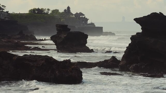 Coastal Bali Temple Silhouette Above Ocean, Misty Horizon With Layered Cliffs And Lush Green Foreground, Traditional Meru Shrine Roofs Rising From Rock Outcrop, Tranquil Sunset Tones And Spiritual