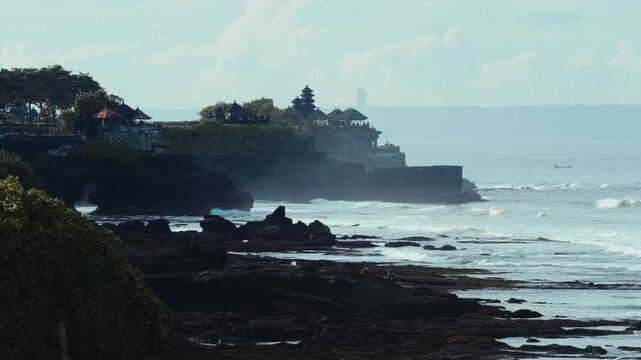 Tanah Lot Temple On Rocky Cliff Dawn, Gentle Waves And Mist Roll Against Sacred Outcrop Cinematic Drone Framing Shows Shrine Silhouette Under Soft Tropical Light, Ideal For Travel, Spiritual place