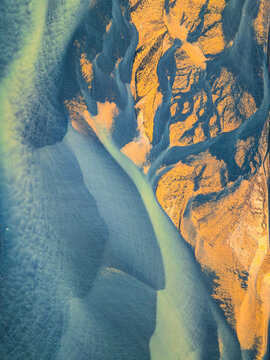 Aerial view of a braided river system featuring intricate patterns of glacial sediment, vibrant blue-green water, and golden-brown sandbanks, Iceland.