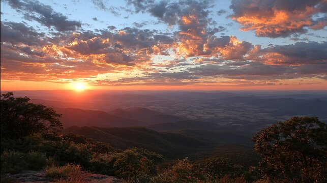 Breathtaking high-altitude view of sun rising over misty mountain range with scattered dark clouds and colorful dawn sky