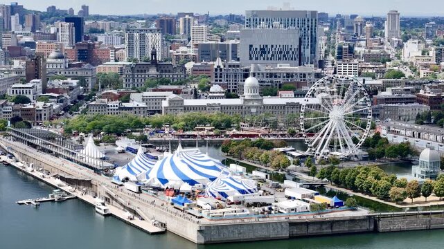 24th of June 2026 drone flight above the Cirque du Soleil blue-white tent at Montreal Old Port with city skyline in background. g.