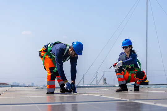 Technicians in safety harness installing solar panels on rooftop, Renewable energy team working together on solar photovoltaic system installation, Workers installing solar panels on building roof