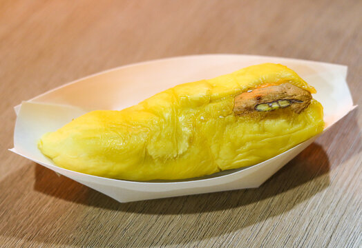 A single, vibrant yellow durian served in a disposable white paper boat.