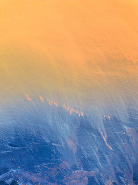 Aerial view of the rugged Icelandic landscape featuring a dramatic transition from golden sunset light to deep blue shadows across volcanic terrain in Iceland.