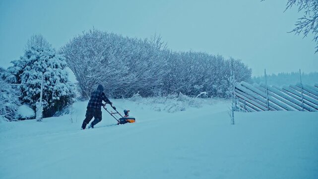 Man Pushing Snowblower Over Extreme Snow-Covered Landscape In A Snowstorm. Wide Shot