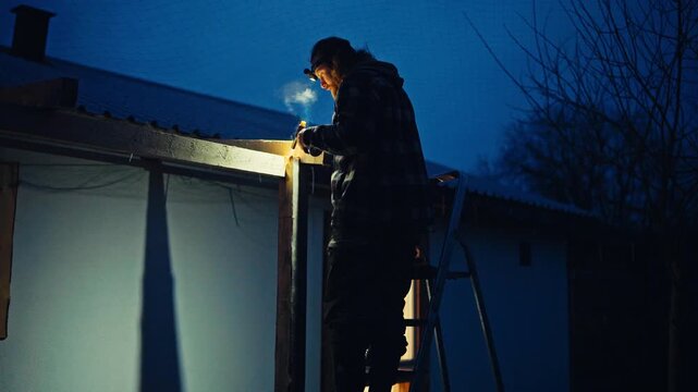 A Man is Working at Night Using a Lighted Tool While Repairing the Roof - Medium Shot
