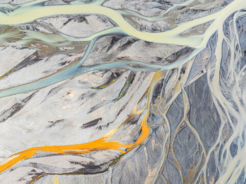 Aerial view of a complex braided river system with glacial meltwater and colorful mineral deposits flowing through the volcanic landscape of Iceland.
