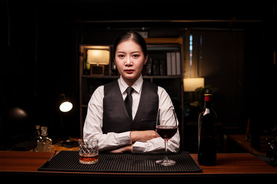 Professional female bartender standing behind counter with alcohol drinks 