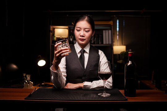 A professional female bartender holds a crystal glass containing red wine on the bar counter.
