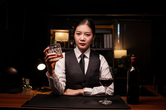 Female Bartender Holding Glass of Whiskey Behind Luxury Bar Counter