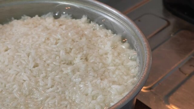 Overhead video of white rice in a metal cooking pot placed on a gas stove top, representing everyday home cooking and staple Asian food preparation.