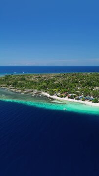 Vertical drone pans right and flies over Public Pamilacan Beach, revealing white sand, reef, village, and blue water in Pamilacan Island, Bohol