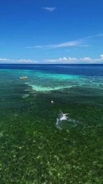 Vertical drone flies over swimmers, then orbits a kayaker and snorkelers above the coral reef near Public Pamilacan Beach