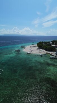 Vertical drone ascends from Public Pamilacan Beach and pans right, revealing Pamilacan Island, reef, boats, and Bohol Sea