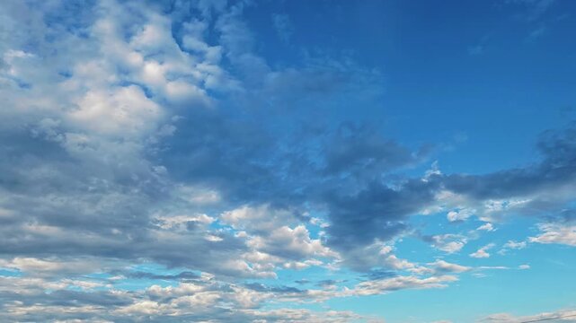 A vibrant blue sky is filled with patchy, scattered white and grey cumulus clouds. Moving dynamically, this cinematic stock footage is perfect for video backdrops, transitions, or nature projects.