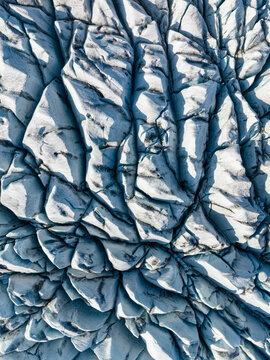 Aerial view of the intricate patterns of deep blue crevasses and jagged ice formations on a glacier surface in Iceland.