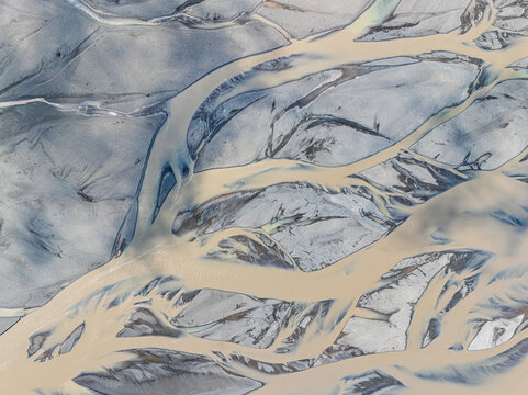 Aerial view of a braided river with intricate glacial water channels and grey sediment banks in Iceland.