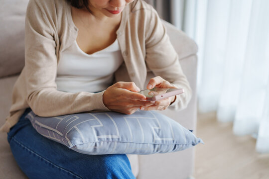 Young Asian woman relaxing and using mobile phone on a sofa at home in the morning