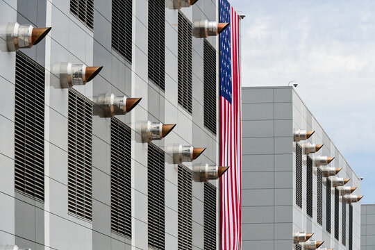 Data center exterior with rows of ventilation vents and cooling infrastructure, with an American flag displayed on the facade, illustrating digital infrastructure and technology