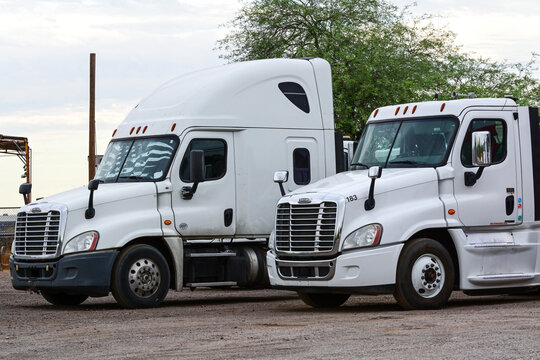 Two Freightliner semi truck tractors parked at an industrial lot, illustrating commercial trucking, freight transportation, logistics, fleet operations, and supply chain infrastructure