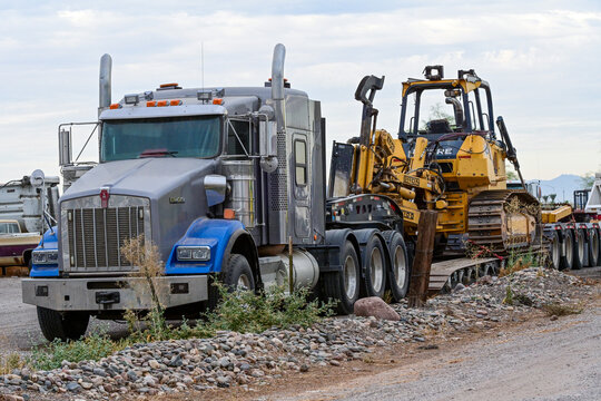Heavy haul semi truck transporting a Caterpillar bulldozer on a lowboy trailer at a construction yard, representing equipment logistics, heavy transport, and infrastructure development support