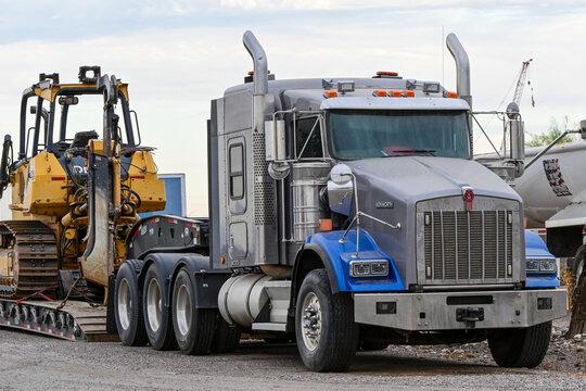 Kenworth semi truck tractor parked with heavy construction equipment at an industrial lot, illustrating commercial trucking, equipment transport, logistics, and construction operations