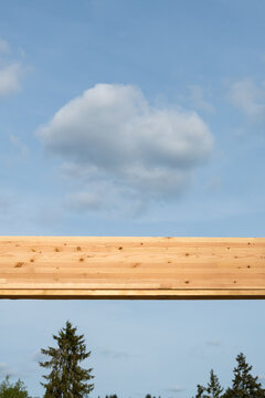 Overhead wood glue laminate, glulam, header beam with blue sky and puffy white clouds in background and fir trees below, housing development project under construction
